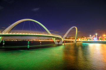 Fototapeta premium Elizabeth Quay Bridge by night on Swan River at entrance of Elizabeth Quay marina. The arched pedestrian bridge is a tourist attraction in Perth, Western Australia. Copy space.