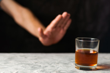 Man hand showing denial and transparent glass with alcohol on gray cement on black background