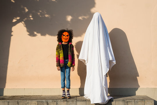 Girl in pumpkin mask holding hand of ghost in the street.