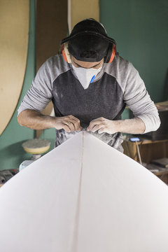 Male shaper working on surfboard stringer in his workshop