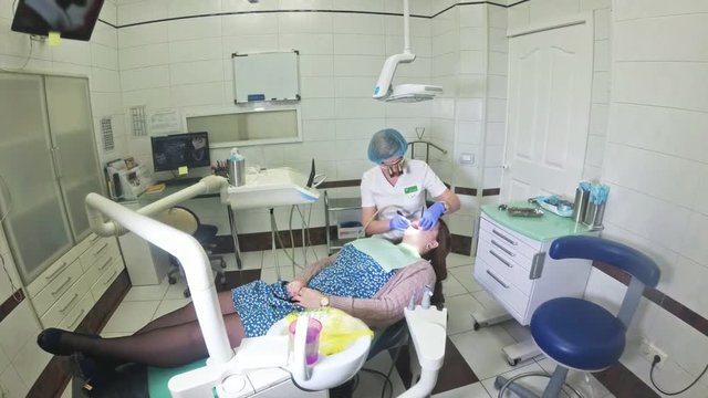 Woman at dentist clinic gets dental treatment to fill a cavity in a tooth. Dental restoration and composite material polymerization with UV light and laser. Shooting at a wide angle.