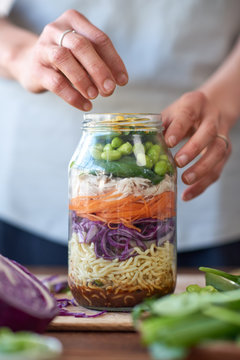 woman hands layering salad ingredients in glass jar