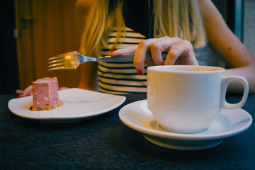 Close-up of a stone table with a cup of coffee and a delicious piece of cake. Model holds the mug and enjoys. Fashionable new interior. Perfect background for websites or coffee shops