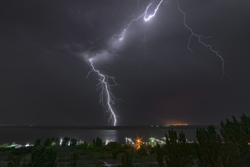 Bright flash of night lightning on the river bank.