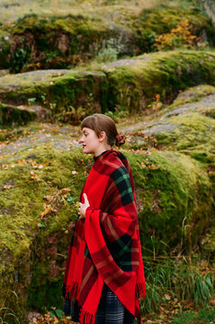 Young woman covered with bright woollen plaid surrounded by stonescovered with moss