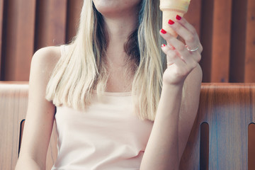 Pretty young girl licks a horn with ice cream on a hot day outdoors. Model deep inside ice cream licking cream. Close-up of long tongue and mouth. Trendy modern style