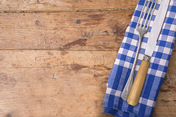 Food rustic background with old fork and knife on blue and white checkered napkin on vintage wooden table