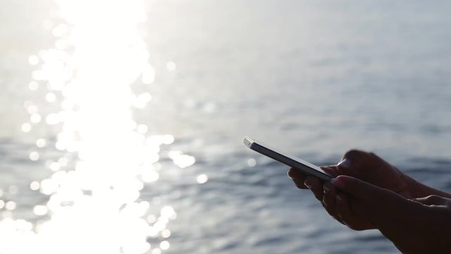 Adult woman using mobile phone on vacation at sea early morning. Tourist texting sms on wifi on beach holidays at bright sunny sunrise background. Real time full hd video footage.