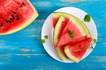 Ripe juicy red watermelon slices on a white plate on a blue wooden background. Top view.