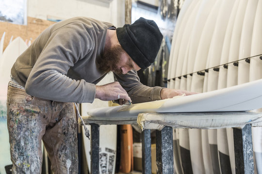 Male shaper focused on surfboard repair