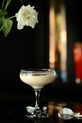 white alcohol cocktail on a black background with a white flower