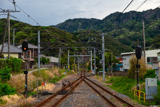 The railway tracks crossing and disappearing among the green covered mountains in the distance, in a small Japanese town Nokogiri not far from Tokyo. The rail traffic light shines yellow in front