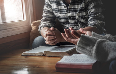 Two christianity sitting around wooden table with open holy bible and praying to God together.