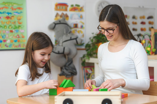 Teacher and child playing with didactic colorful toys indoors - preschool
