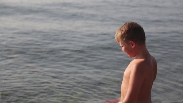 Happy joyful little kid playing in sea splashing blue water with pleasure. Healthy carefree child enjoying summer holidays at beach resort on sunny morning. Real time full hd video footage.