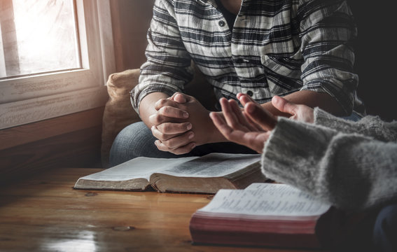Two christianity sitting around wooden table with open holy bible and praying to God together.