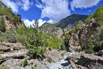 Fototapeta na wymiar Tourists walking along the trail in the Samaria Gorge in Crete. This majestuous gorge is considered one of the great attractions of Crete