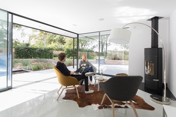 Young couple relaxing in a contemporary room with glass doors open to the garden.