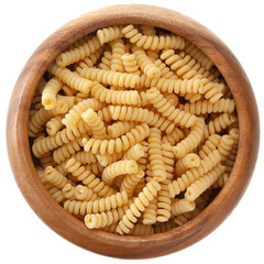 Curly pasta in a round wooden bowl isolated on white background, top view