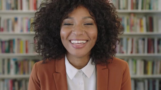 portrait of stylish young african american business woman intern laughing cheerful at camera in library bookshelf background