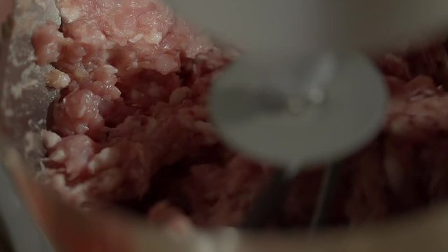 Close up shot of working mixer machine. It is mixing a mincing raw meat. Part of cooking homemade sausages.