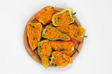 Halves of sweet pepper stuffed with carrots on a round wooden board. White background. Close-up. View from above.
