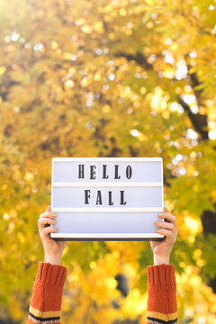 Woman holding hello fall message on light box
