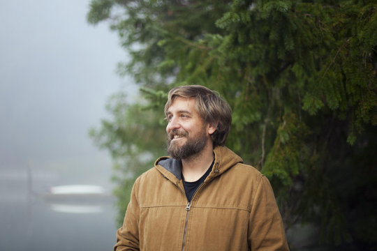 Man in hooded jacket stands on a dock in Fletcher Bay on a foggy morning.