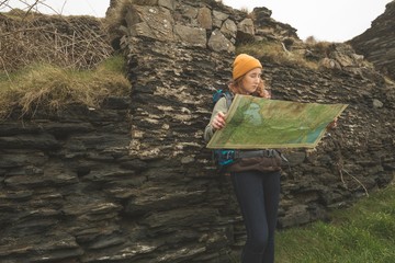 Female hiker leaning against the rock and reading a map