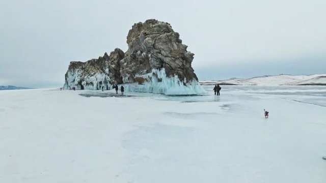 Travel of woman on ice of Lake Baikal. POV view. Trip to winter island. Girl is walking at foot of ice rocks. Traveler looks at beautiful ice grotto. Hiker wears sports glasses, silver jacket