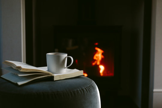 Mug of hot chocolate and book in front of a lit stove