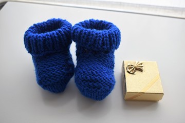 Gifts for a new born baby boy: yellow baby wool shoes, a handmade woven white pullover and a golden gift box