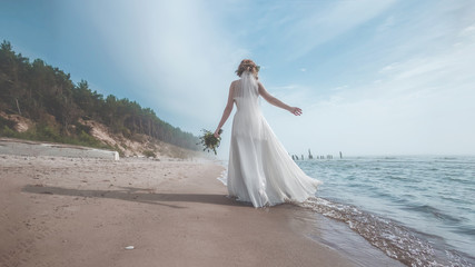 Fototapeta na wymiar bride in white wedding dress standing near the sea on a beach