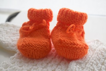 Fototapeta na wymiar Baby Orange wool shoes above a handmade woven white pullover