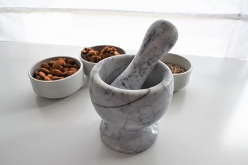 Three white containers with almonds, walnuts and a mixture of sunflower, sesame and chia seeds near a marble mortar.