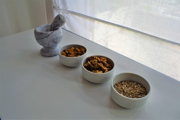 Three white containers with almonds, walnuts and a mixture of sunflower, sesame and chia seeds near a marble mortar.