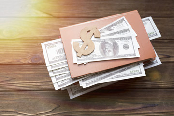 Obraz premium dollar sign, book, dollar bills in the background of a wooden table. business, finance. investment.