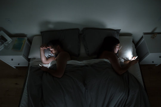 Couple using their phones in bed at night