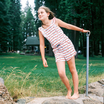 Ten year old girl in stars and stripes romper at a cabin on a windy day