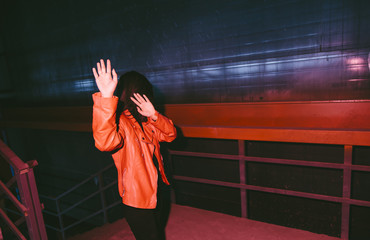 Girl in red jacket hiding face from camera at night