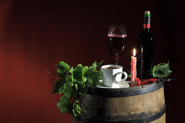 Butelka czerwonego wina i kawa w świetle świecy na beczce z winogronem.