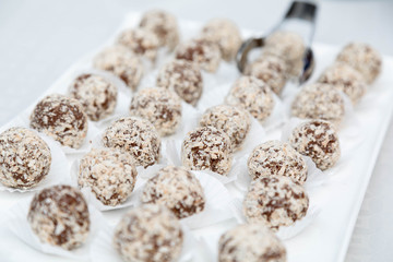Candies from a fig of corpulent work in the form of the balls sprinkled with coconut flakes lie in an open box. One ball is kept in nippers for food. Horizontal shot