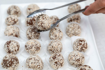 Candies from a fig of corpulent work in the form of the balls sprinkled with coconut flakes lie in an open box. One ball is kept in nippers for food. Horizontal shot