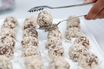 Candies from a fig of corpulent work in the form of the balls sprinkled with coconut flakes lie in an open box. One ball is kept in nippers for food. Horizontal shot