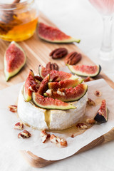 Round brie or camambert cheese on cutting board white with fruits and nuts 
