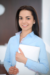 Young brunette business woman looks like a student girl working in office. Hispanic or latin american girl standing straight