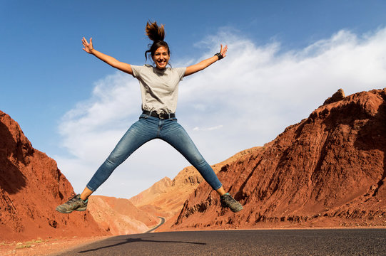 A woman jumping in the air on a desert highway in Morocco - Powered by Adobe