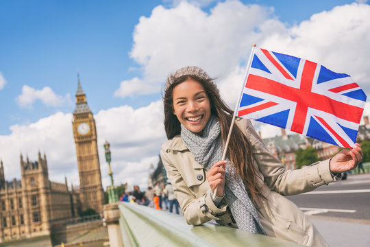 London travel tourist woman showing Union flag Great Britain british UK flag. Asian girl at Big Ben on Westminster bridge on Europe holidays holding icon at iconic landmark.