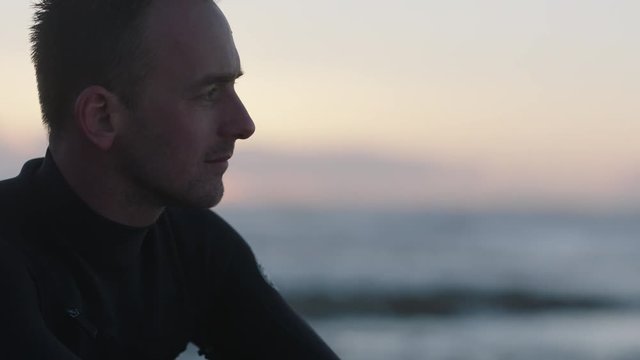 close up portrait of young surfer man sitting on beautiful seaside beach looking pensive contemplative successful male thinking healthy lifestyle goals