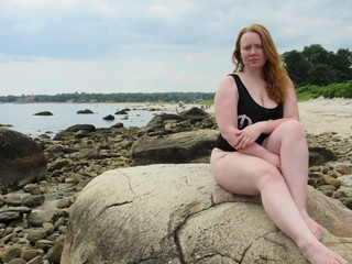 Fototapeta na wymiar A young redheaded woman sitting on a rock at the beach 